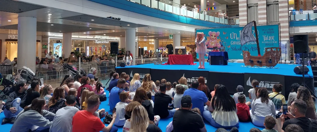 Centro Comercial Añaza Carrefour con espectáculo infantil en el escenario. Familias y niños disfrutan sentados en el suelo mientras observan la actuación.